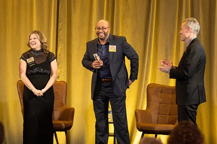 Geraud Blanks accepts a Graduate of the Last Decade award at the 2023 UWM Alumni Awards from Michelle Putz, president of the UWM Alumni Board, as Chancellor Mark Mone applauds.