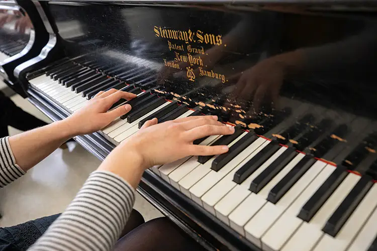 Hands playing a Steinway & Sons grand piano with visible brand name on the instrument.