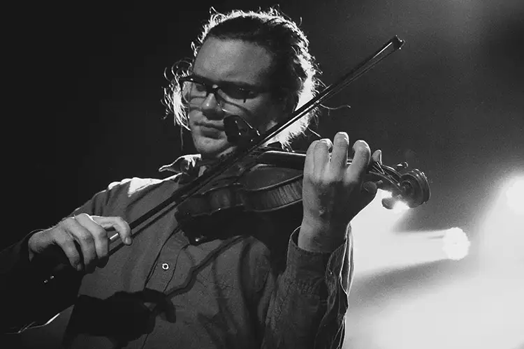 String pedagogy masters student playing a violin on stage under bright lights, captured in black-and-white.