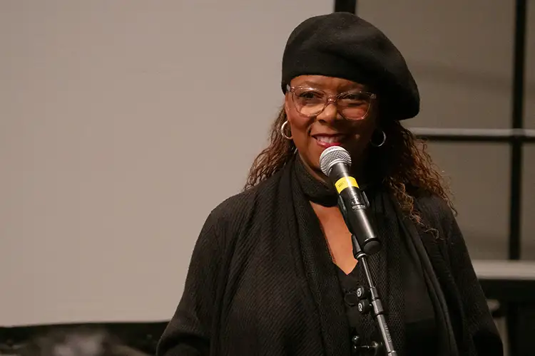 Patrice Rushen in black clothing speaks into a microphone in an indoor event space.