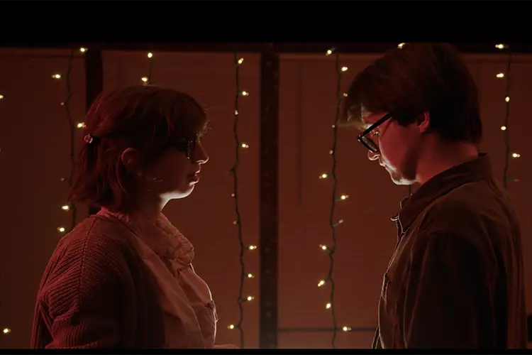 A man and a woman stand opposite of eachother infront of string lights A man and a woman stand opposite of eachother infront of string lights