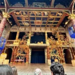 An ornate theater stage with painted ceilings, tall decorated columns, and golden tree‑like set pieces, viewed from the audience.