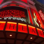 Bright red and neon‑lit theater facade advertising Stranger Things: The First Shadow at night.