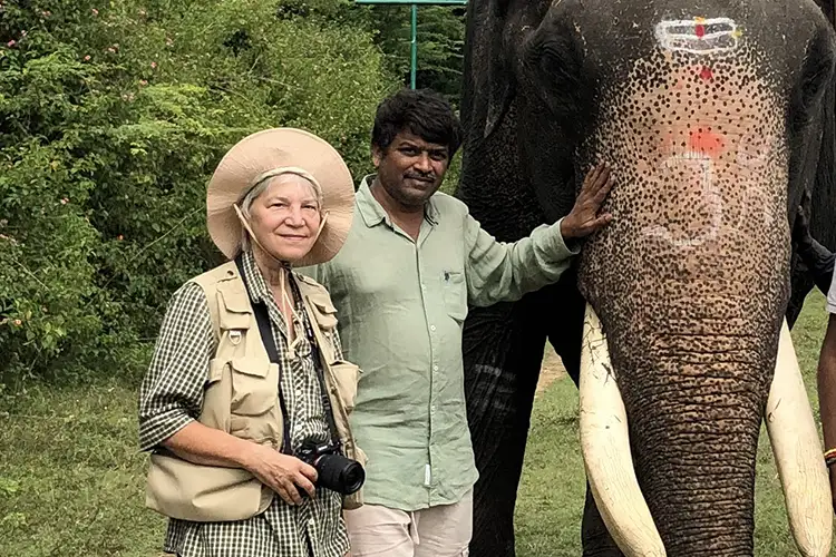 Lenore Rinder and Vallish Kaushik stand beside a decorated elephant in a green outdoor setting.
