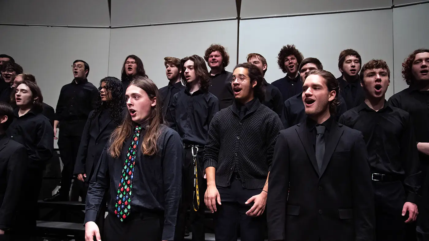 Choir of students in black attire singing on risers during concert performance.