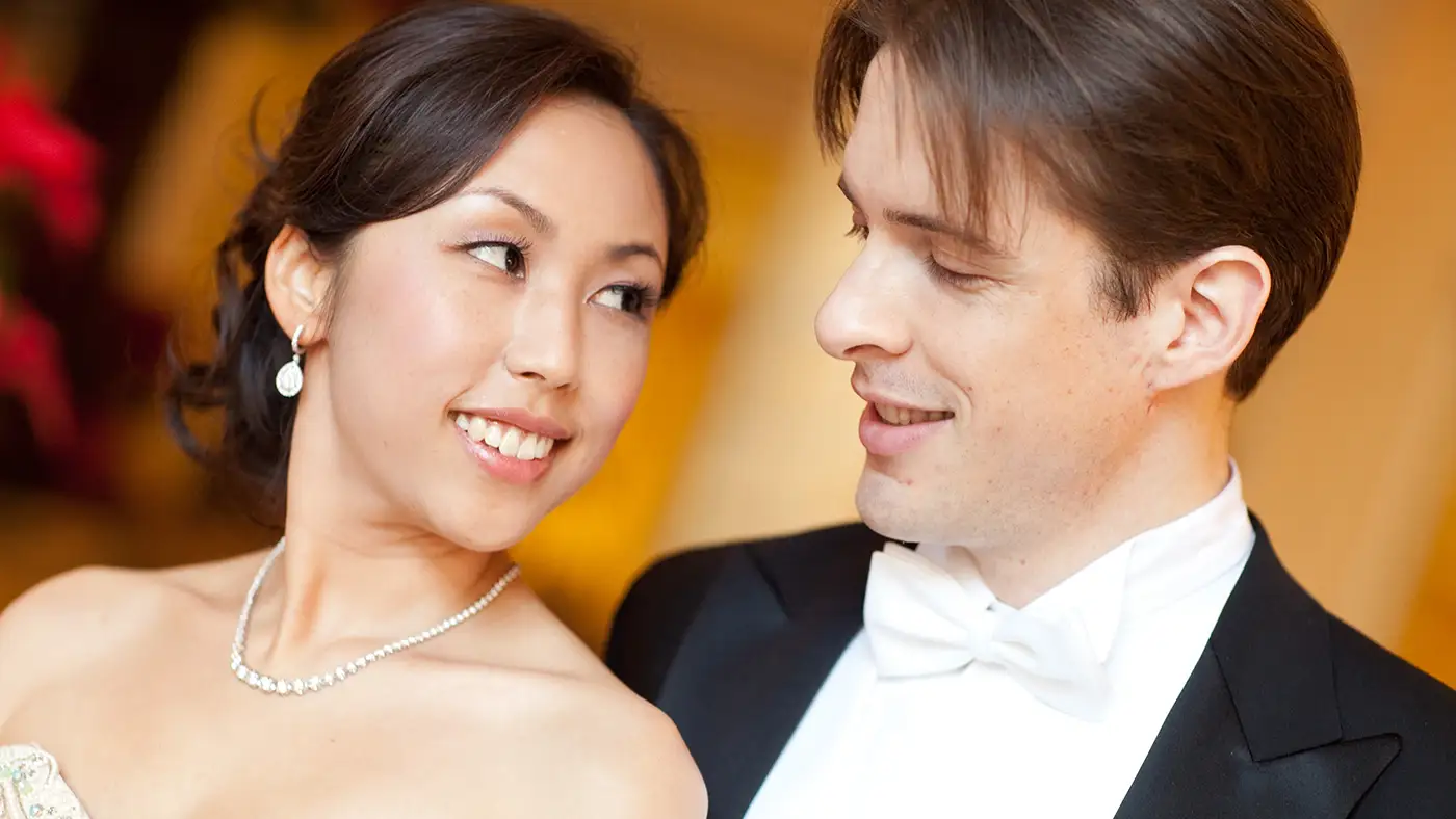 Close-up portrait of two formally dressed performers in concert attire, facing one another under warm lighting.