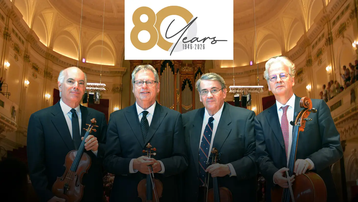 The Fine Arts Quartet stand while holding their stringed instruments on a concert hall stage.