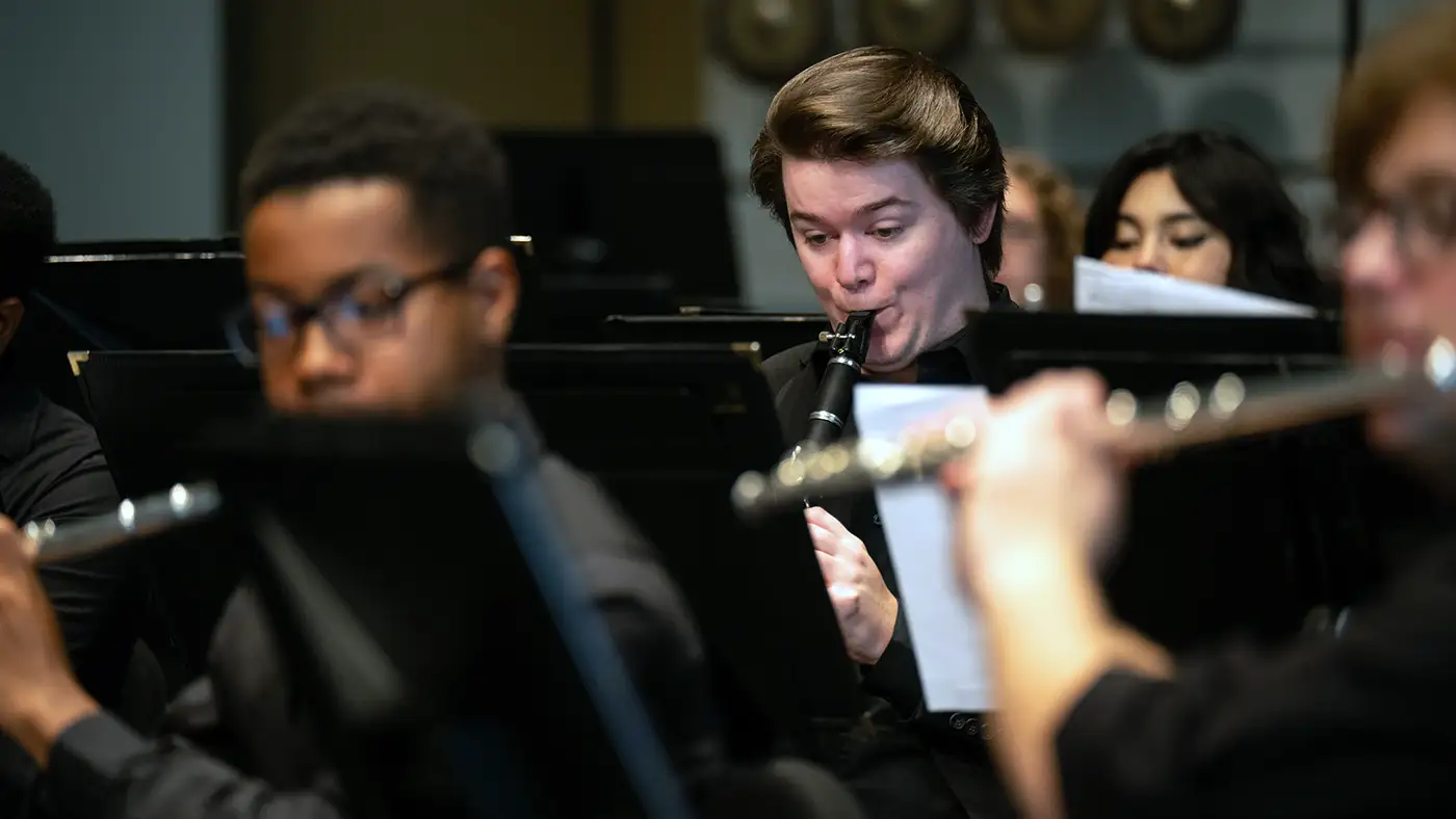 Clarinet player in concert band, with flutes and other musicians blurred in foreground.