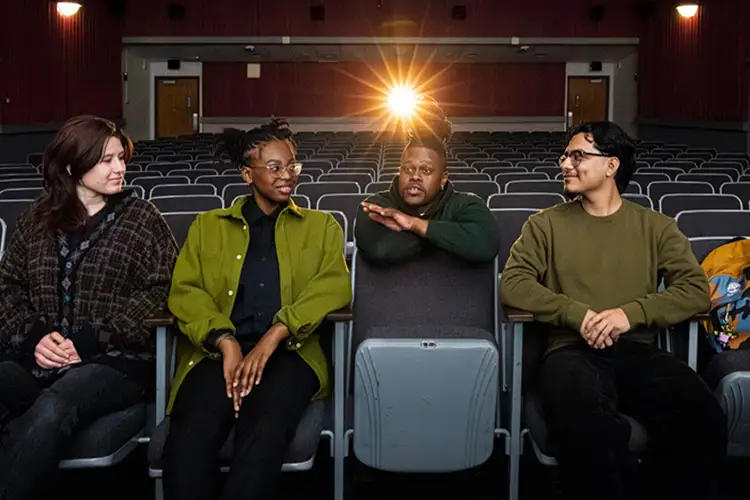 Four people seated in a theater with a bright projector light behind them.