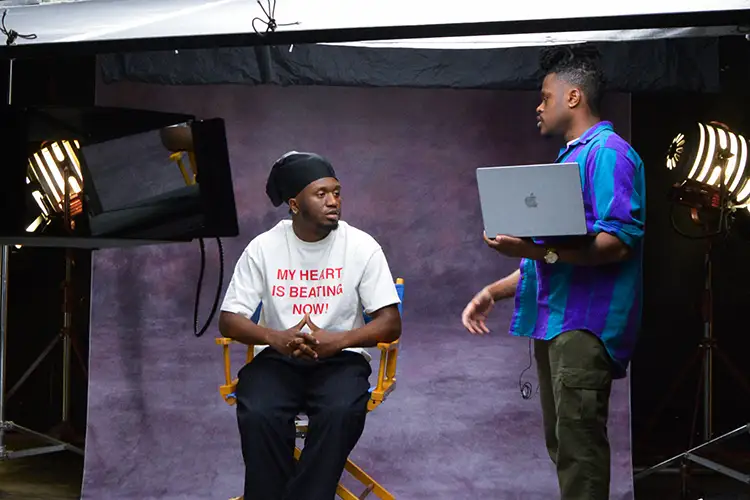 Behind-the-scenes view of a film set with two people, studio lights, and a laptop
