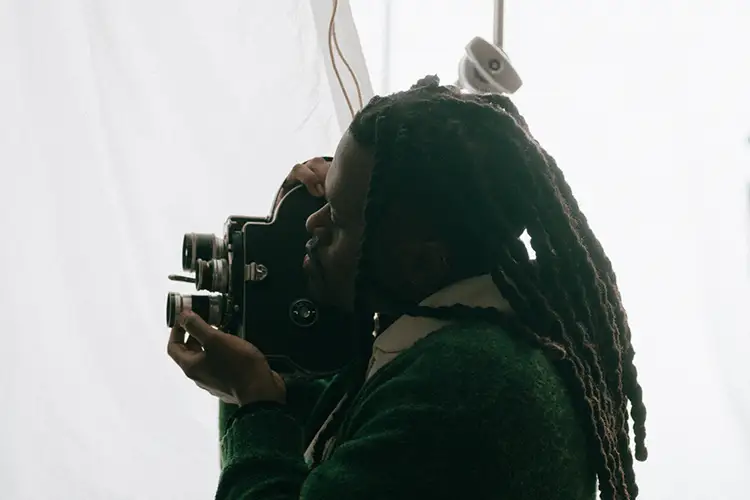 Marquise Mays operating a vintage film camera in a bright studio setting.