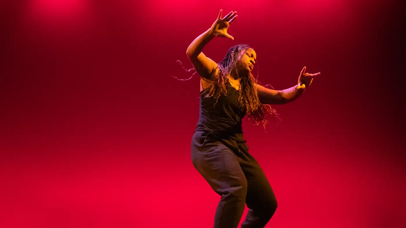 UWM Dance student dancing on stage under vibrant red lighting.
