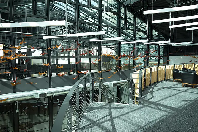 Interior of a modern industrial building with many orange bird sculptures hanging from the ceiling