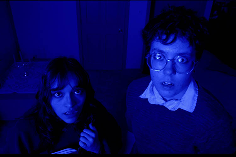 Two people look upwards while being cast in dark blue light