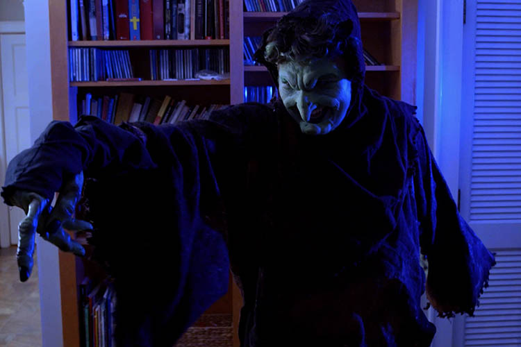 The witch points off to the left of the screen, drenched in blue light