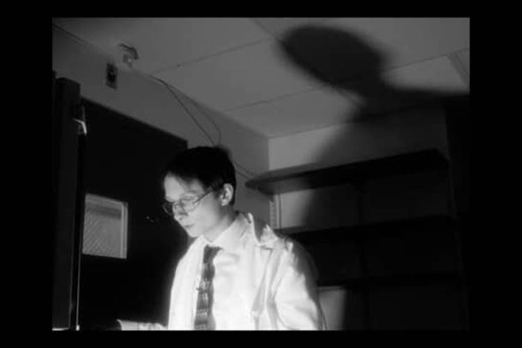 The light of the computer casts a scientist's shadow on the wall behind him.