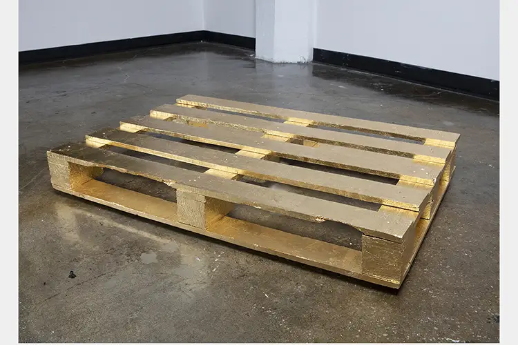 Wood palette on a cement floor covered in gold leaf