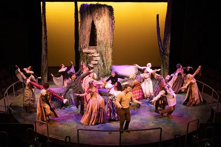 Actors perform on a circular stage in a dynamic scene inspired by Chris Guse’s theatrical stage design.