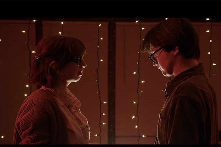 A man and a woman stand opposite of eachother infront of string lights