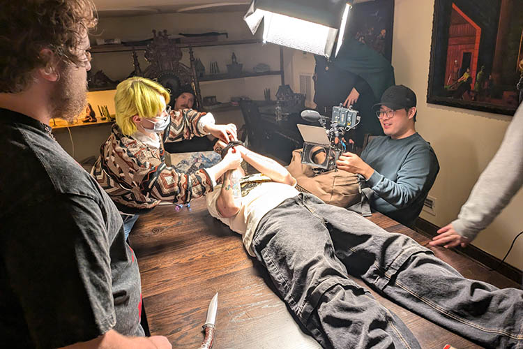 The crew helps an actor bind his hands together as the prepare to film the next scene