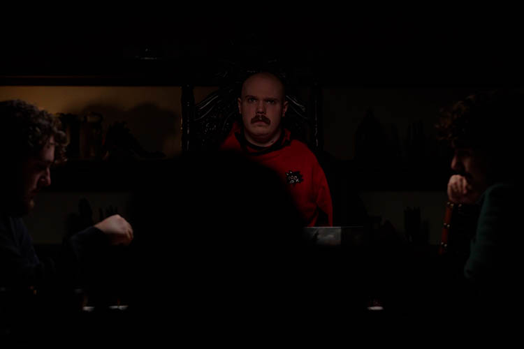 A man looks listlessly to others in a dimly lit room