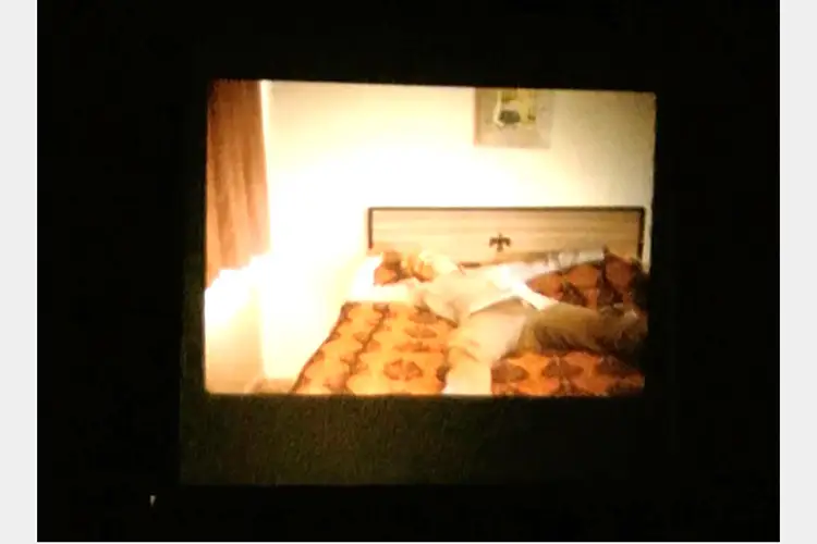 Film still of a bedroom with a man lying on his back on the bed.