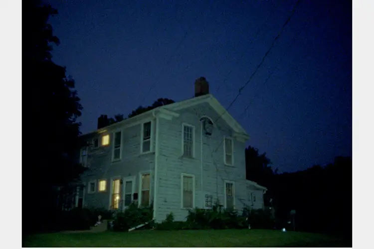 View of side of a house in late evening with three windows lit up from inside
