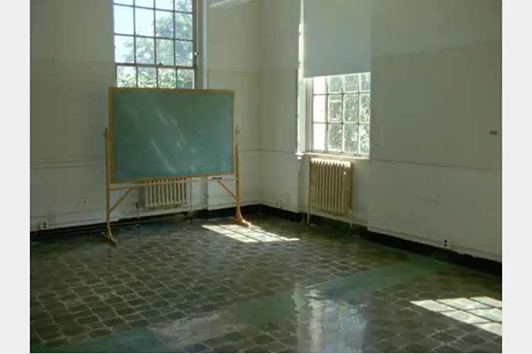 An empty classroom with two windows and a blank rolling chalkboard