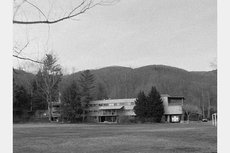 Black and white image of a building taken from a distance, hills in the background
