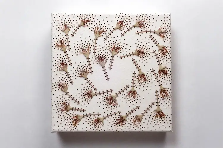 Square white textile artwork with dotted surface and stitched dried flowers forming a spiral pattern