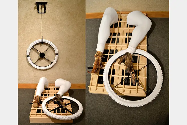Suspended plaster cast bike tire with prosthetic legs laying on a wooden palate
