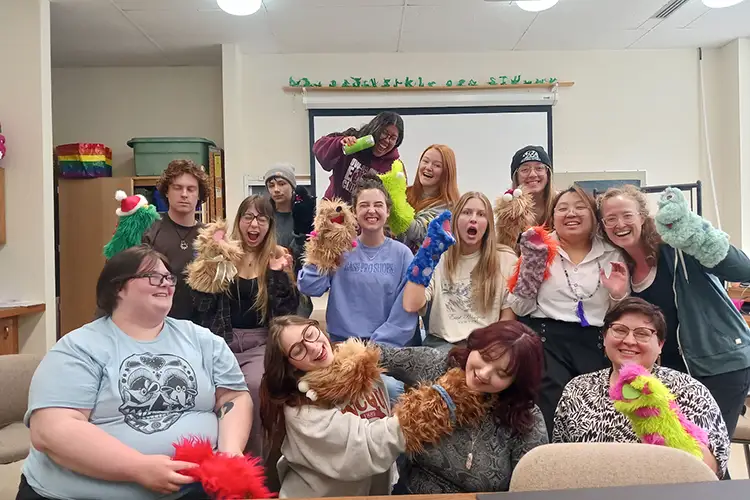 Liz Rex, Debra Hardy, and Art Education students all huddled in a group photo, showing off their puppets