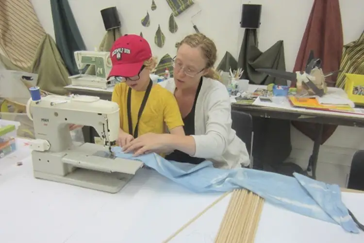 Liz Rex showing a young child how to use a showing machine. They are stitching light blue fabric.