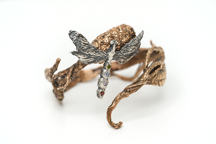A bracelet with a golden band with a silver dragonfly in the middle.