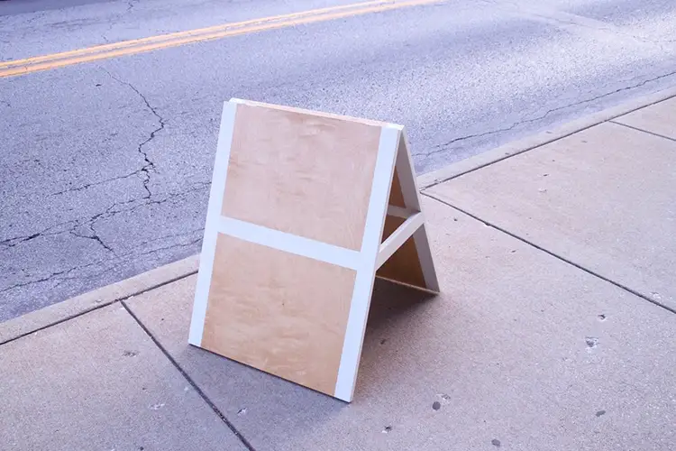 A blank, wooden sign clapboard sitting on the edge of the sidewalk