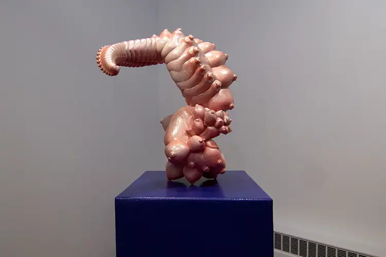 Amorphous sculpture resembling the flesh-colored, morphing body of a bug on a blue pedestal Amorphous sculpture resembling the flesh-colored, morphing body of a bug on a blue pedestal