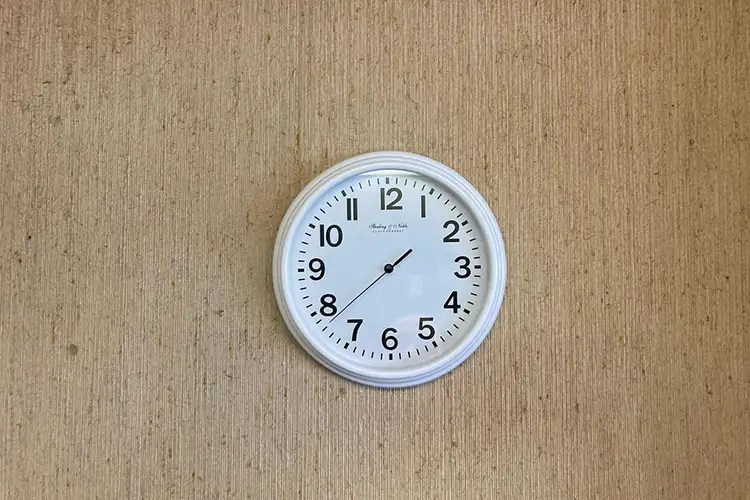 A white clock with only a second hand, pointing just before 8, hung on a bare wooden wall