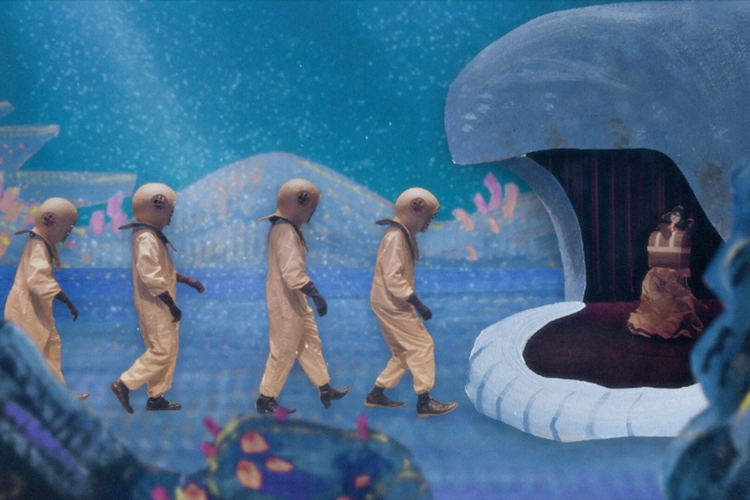 Four men in golden submarine suits walk past corals towards a whale's open mouth. 