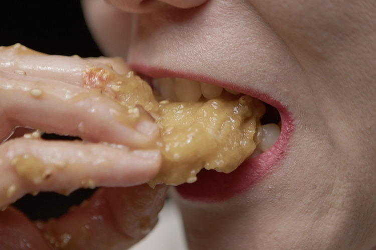 A pale woman eats a chicken dish, sloppily. 