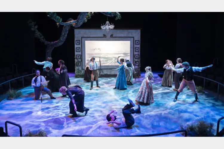 Ensemble cast performs on a theater stage with ocean-like floor projection, tree and framed backdrop, dancers and actors in varied poses. Ensemble cast performs on a theater stage with ocean-like floor projection, tree and framed backdrop, dancers and actors in varied poses.