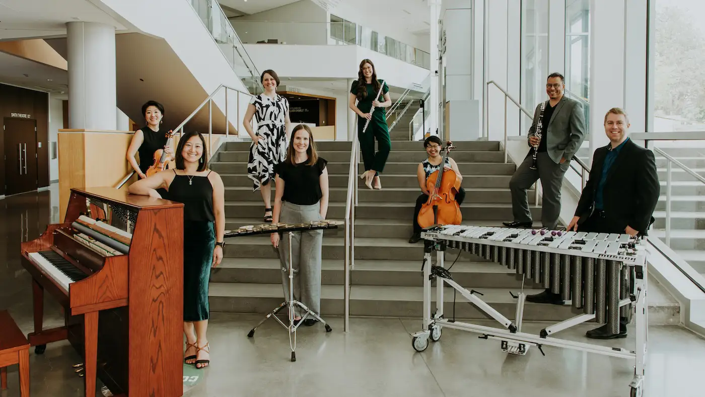 Khemia Ensemble musicians pose on a grand staircase with piano, strings, woodwinds, flute, and vibraphone.