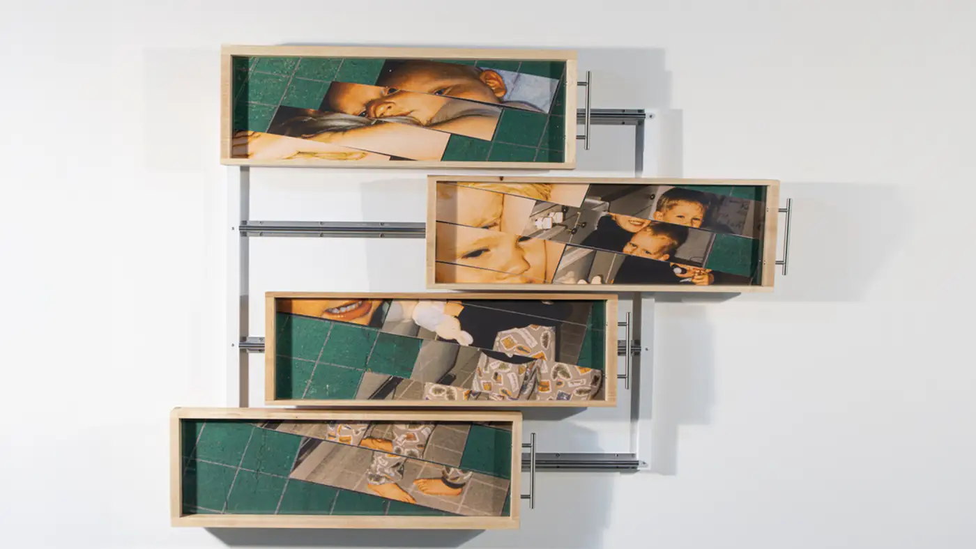 Wall-mounted mixed-media artwork composed of four sliding framed panels displaying fragmented family photographs, arranged on a metal track system that reveals shifting image combinations.
