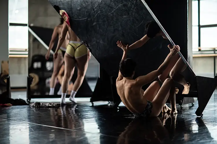 Contemporary dancers interact with large reflective panels in a bright rehearsal studio.