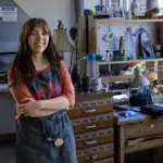 Barden smiles at the camera while leaning against a workbench with her arms crossed.
