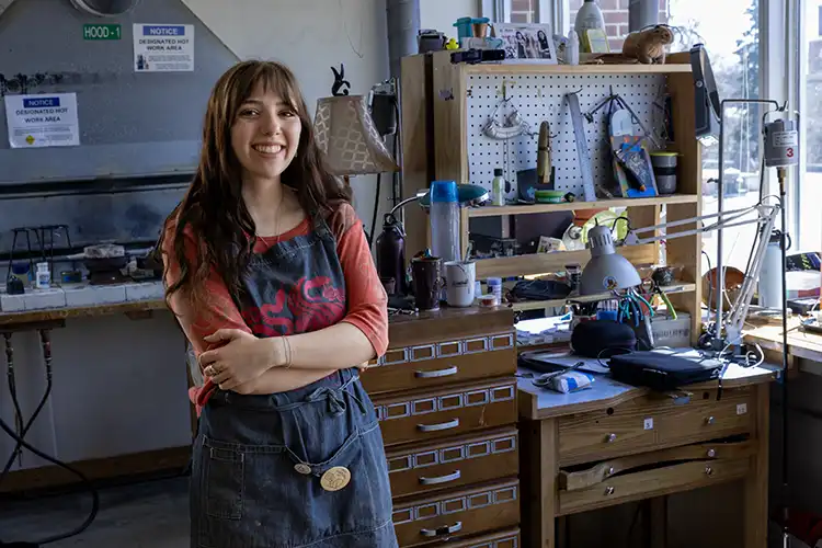 Barden smiles at the camera while leaning against a workbench with her arms crossed.