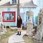 Harris stands in front of a light green house surrounded by sculptures