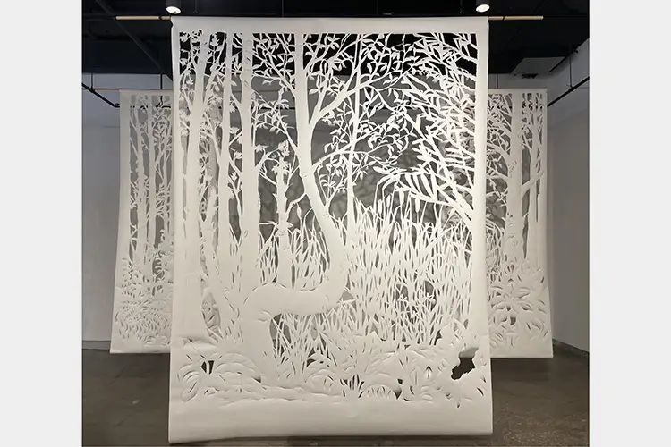Three large tapestries of cut paper hanging from the ceiling showing woodland nature scenes, one in foreground and two in background Three large tapestries of cut paper hanging from the ceiling showing woodland nature scenes, one in foreground and two in background
