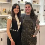 Omick and Burrows smile in front of shelves lined with their art in their shop.