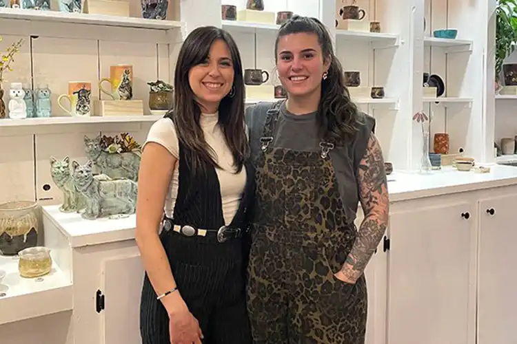 Omick and Burrows smile in front of shelves lined with their art in their shop.