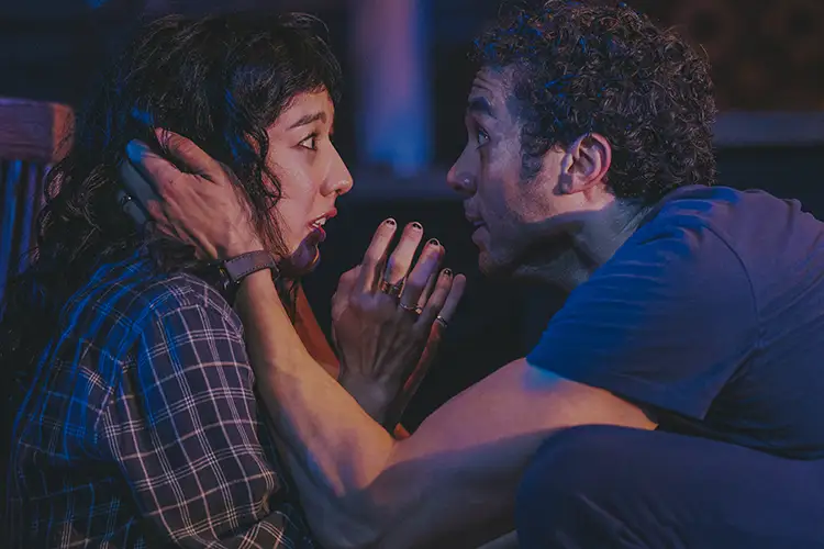 Close-up of two people facing each other indoors under blue and purple lighting.